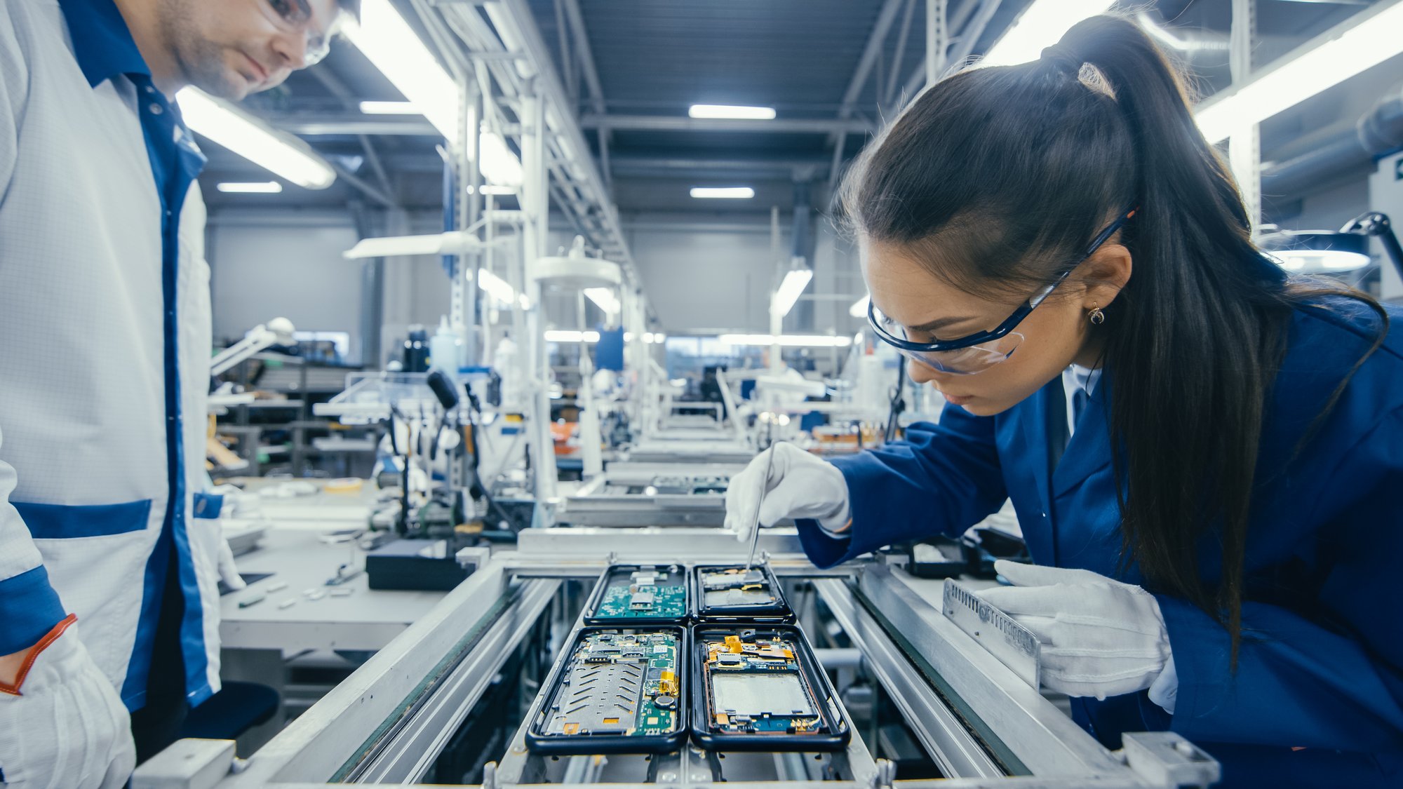 Shot of an Electronics Factory Workers Assembling Circuit Boards by Hand While it Stands on the Assembly Line. High Tech Factory Facility.